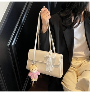 Detail of beige underarm bag with lace bow, plush bear charm, and dual slim shoulder straps