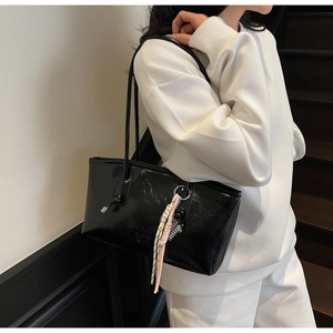 Side view of black glossy patent leather tote bag featuring a decorative woven charm