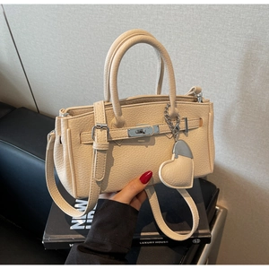 Detail of beige lychee pattern handbag with silver lock and heart-shaped pendant charm