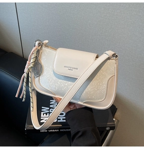 Close-up of cream square bag with scale texture and silver tennis racket pendant detail