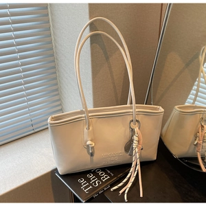 Détail d'un sac à main en similicuir crème avec logo embossé et breloque en corde tressée