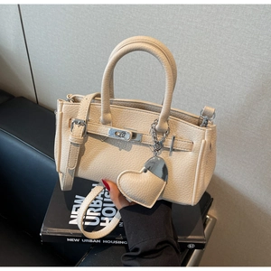 Detailed shot of beige lychee grain leather handbag with top handle and heart charm