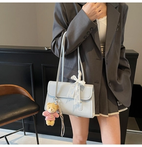 Detail of light blue patent leather handbag with a white lace bow and a cute bear charm