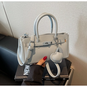 Detail of grey lychee leather handbag with metal lock and heart-shaped pendant