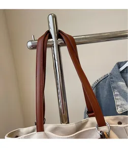 Detalle de bolso tote de lona con asa de cuero marrón y anillo de metal plateado