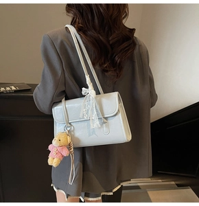 Side view of light blue leather shoulder bag with plush bear and lace bow charms
