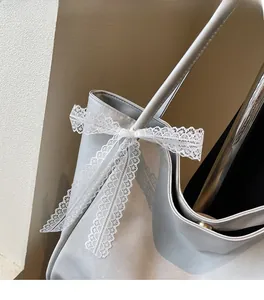 Detail of grey leather tote bag featuring a delicate white lace bow and rivet accents
