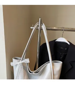 Detail view of smooth silver tote bag featuring a white lace bow and slim straps