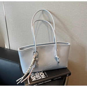 Detail of light blue tote bag with embossed logo and colorful braided tassel charm