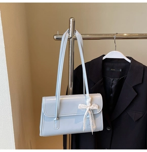 Close-up of light blue patent leather shoulder bag with white lace bow charm detail