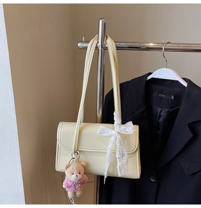 Detail of cream underarm bag with lace bow and cute teddy bear charm on metal hanger