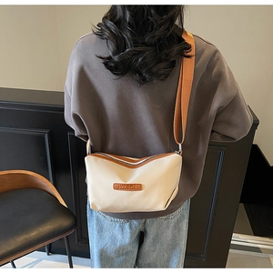 Detail of oxford fabric crossbody bag with leather trim and wide strap on model