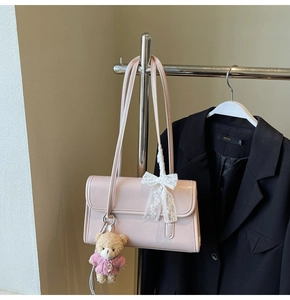 Pink patent leather shoulder bag detail with white lace bow and plush bear charm