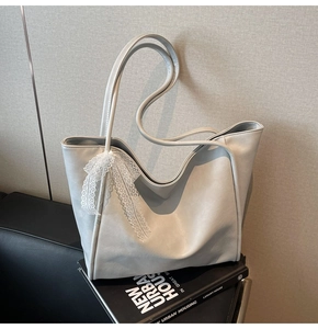 Detail of grey soft leather tote bag featuring a white lace bow and long handles