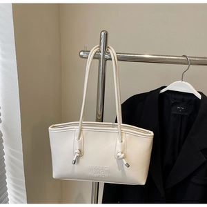 Détail du sac cabas crème avec logo embossé et bandoulière à nœud unique sur l'attache