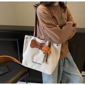 Detalle de bolso tote de lona con parche de cuero y amuleto de perro de peluche