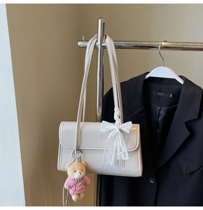 Detail view of beige leather shoulder bag with white lace bow and plush bear charm