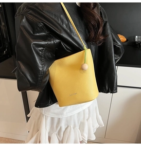 Detail of yellow lychee textured leather bucket bag with CLAROK logo and wooden charm
