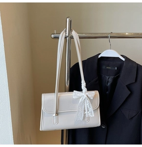 Detail view of cream patent leather underarm bag with a white lace bow accessory
