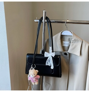 Detail of black patent leather shoulder bag with white lace bow and plush bear charm
