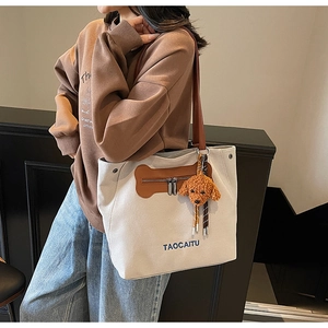 Detailed view of canvas tote bag with brown leather straps and puppy plush charm