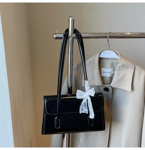 Detail of black patent leather underarm bag with a white lace bow charm on a hanger