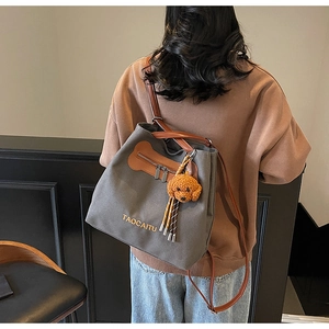 Model wearing a large grey canvas tote bag with brown leather straps and plush charm