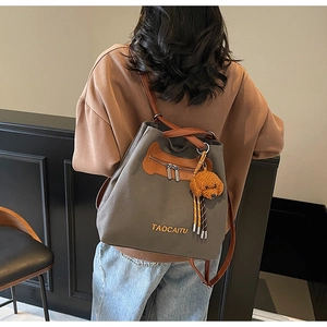 Close-up of grey canvas backpack with leather trim and brown teddy bear charm
