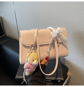 Detail of pink patent leather shoulder bag featuring a lace bow and plush bear charm