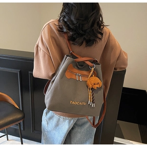 Rear view of a grey canvas backpack with brown leather base and a cute dog pendant