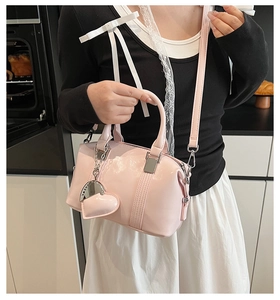 Close-up of pink Boston bag with heart charm and detachable strap in lifestyle setting