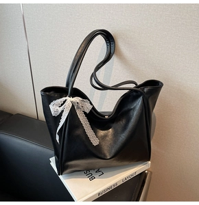 Detail of a black PU tote bag featuring a white lace bow on the handle base