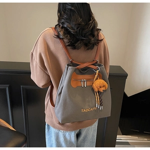 Detail of grey canvas backpack with brown leather trim and a cute puppy plush charm