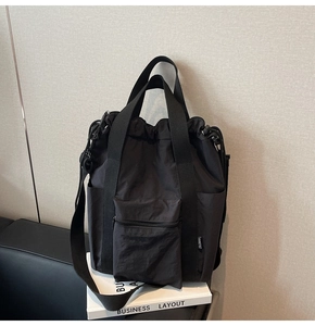 Detail of black nylon tote bag featuring front zip pocket and sturdy shoulder straps