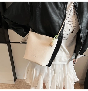 Detail of a creamy white bucket bag with pebble leather texture and green beaded tassel