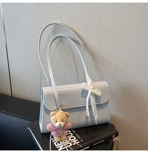 Detailed view of light blue glossy leather shoulder bag with bear charm and lace bow