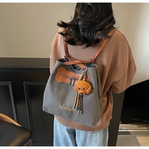 Detalle de mochila de lona gris con cuero marrón y llavero de perrito de peluche
