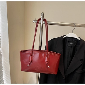 Gros plan d'un sac cabas en cuir verni rouge foncé avec détail de nœud et gaufrage