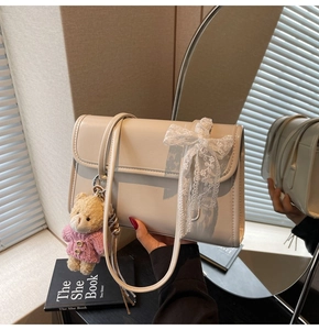 Detail of cream shoulder bag with white lace bow and cute teddy bear plush charm