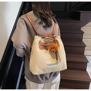 Detail of the cream canvas backpack with brown leather straps and teddy bear charm
