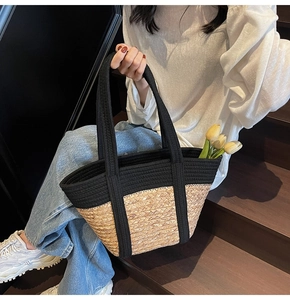 Détail d'un sac cabas en paille tissée avec bordure en toile noire porté par un mannequin