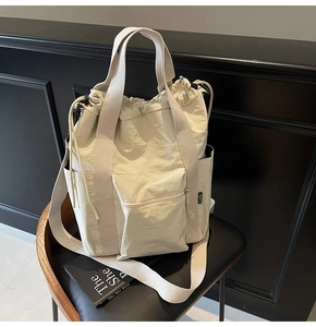 Detail of beige nylon drawstring tote bag featuring a front zipper pocket on a chair