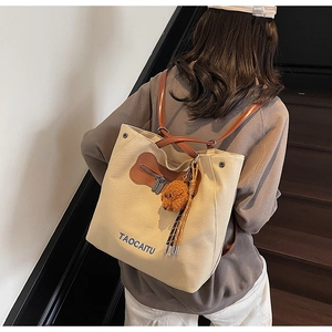 Close-up of beige canvas tote bag with brown leather straps and a plush bear charm