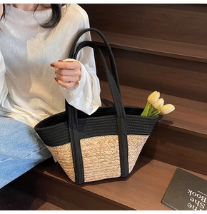 Détail du sac cabas en paille tissé main avec anses en tissu noir sur escalier