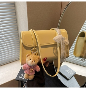Detail of pale yellow leather shoulder bag featuring a cute bear plush and lace bow