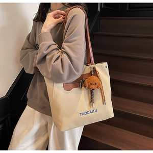 Detail of canvas tote bag with brown leather handles and teddy bear charm on stairs