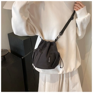 Detail of nylon bucket bag with adjustable strap and side mesh pocket worn by model