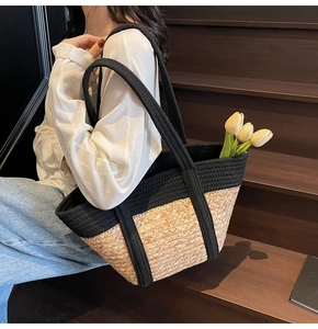 Detailed texture of straw woven tote bag with black contrast strap on wooden stairs