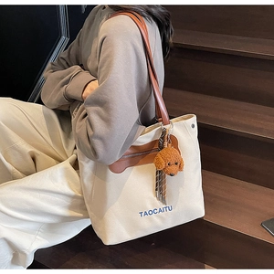 Detail of beige canvas tote with leather straps and a plush puppy charm on stairs