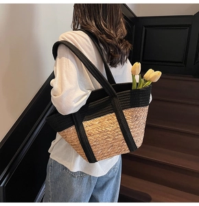 Détail d'un sac cabas bicolore en paille tressée porté par une personne sur un escalier